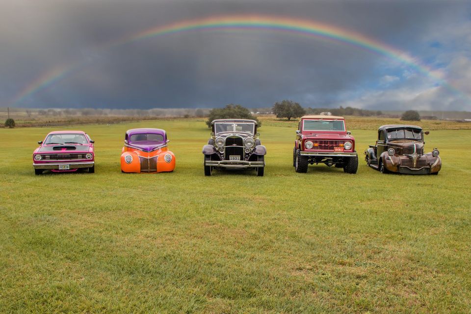 photo of classic cars in field with rainbow above